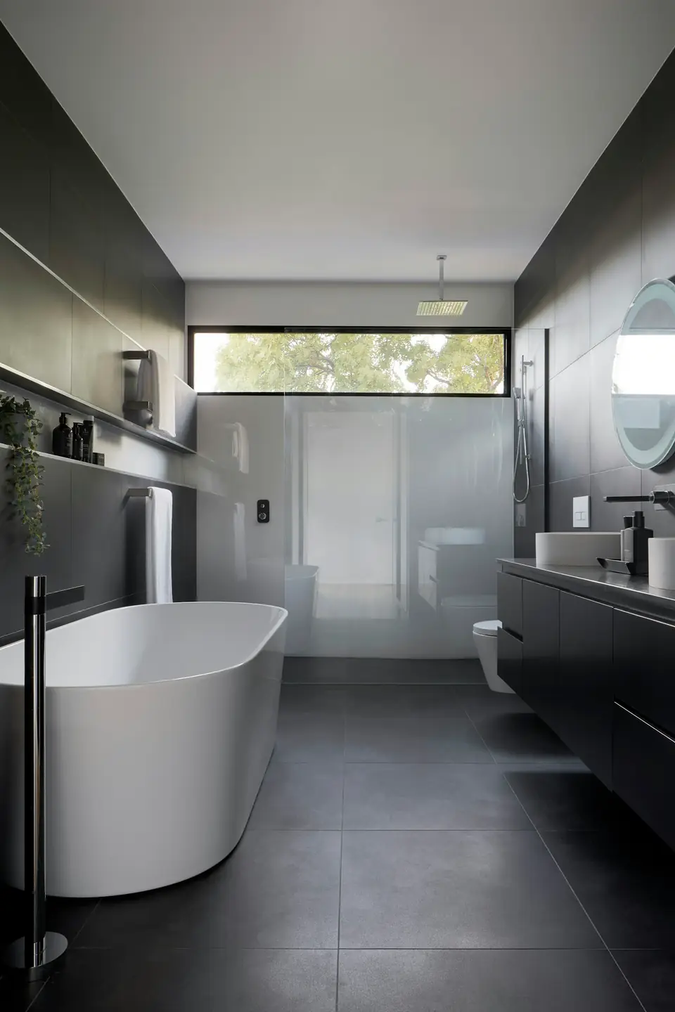 Dark stone bathroom with freestanding tub and garden view